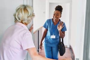 Soignante souriante saluant une femme âgée